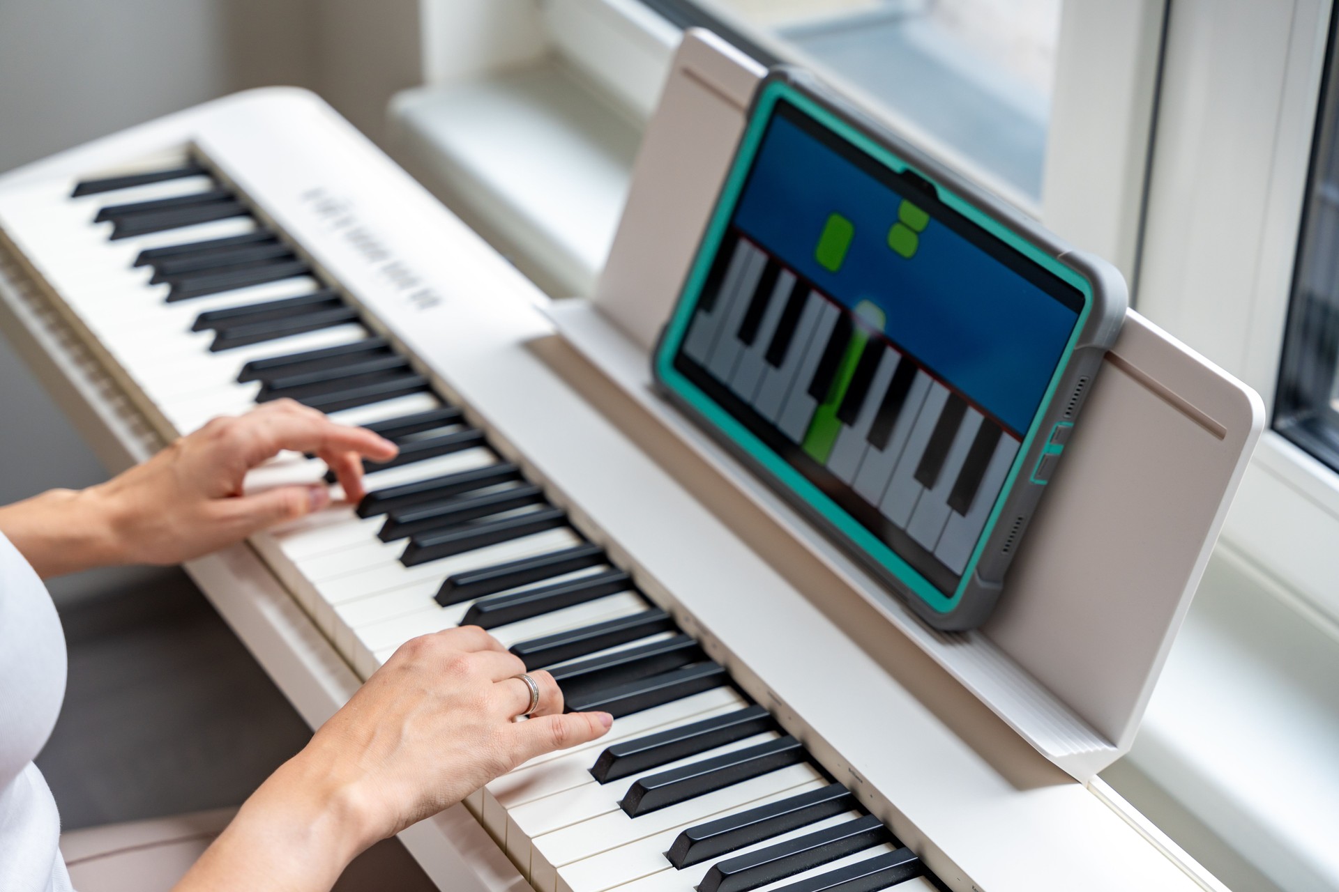 Hands playing a keyboard while following an interactive learning app on a tablet. Technology enables self-education in music without traditional lessons.